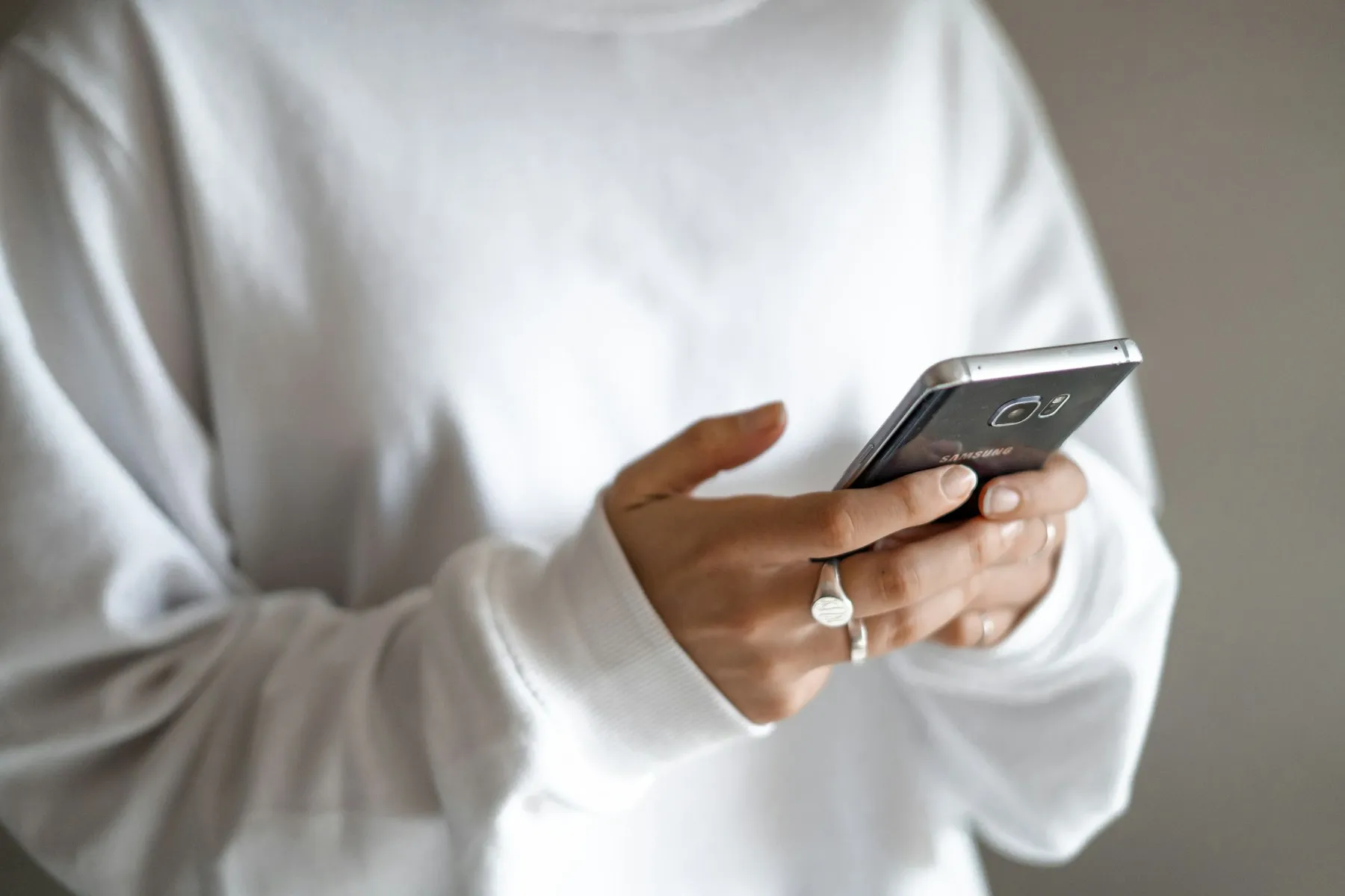 A person in a white sweater holding a smartphone